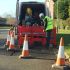 A man in a yellow vest is repairing a section of the road, focused on his work amidst construction equipment.