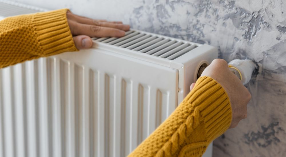A person holds a heating radiator, demonstrating its size and design in a home setting.