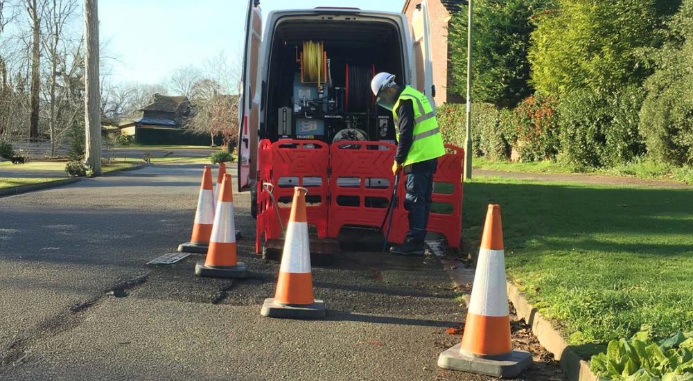 A man in a yellow vest is repairing a section of the road, focused on his work amidst construction equipment.