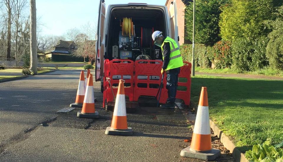 A man in a yellow vest is repairing a section of the road, focused on his work amidst construction equipment.