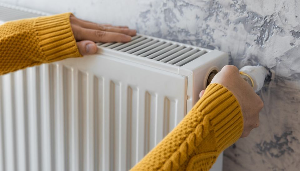A person holds a heating radiator, demonstrating its size and design in a home setting.