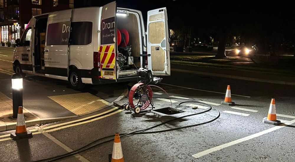 Gaswise company van parked at night beside an open street drain with maintenance equipment and traffic cones set up for drainage work.